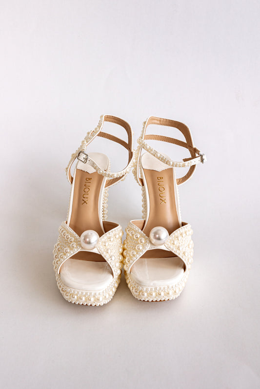 Pair of white high-heeled platforms with pearl embellishments and ankle strap